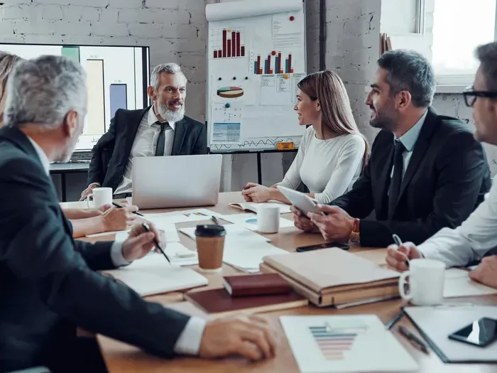 Business executives in a modern boardroom discussing growth charts and strategy, laptops visible